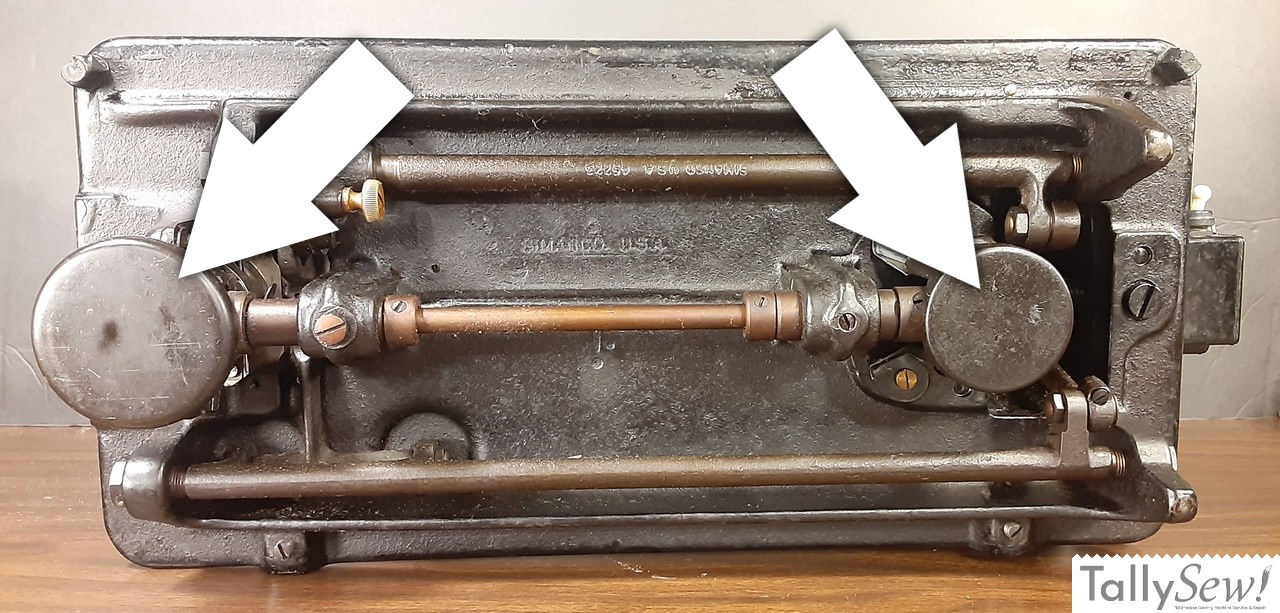 An underside view of a Singer 201-2 sewing machine, with two annotated arrows indicating the locations of the protective gear covers.